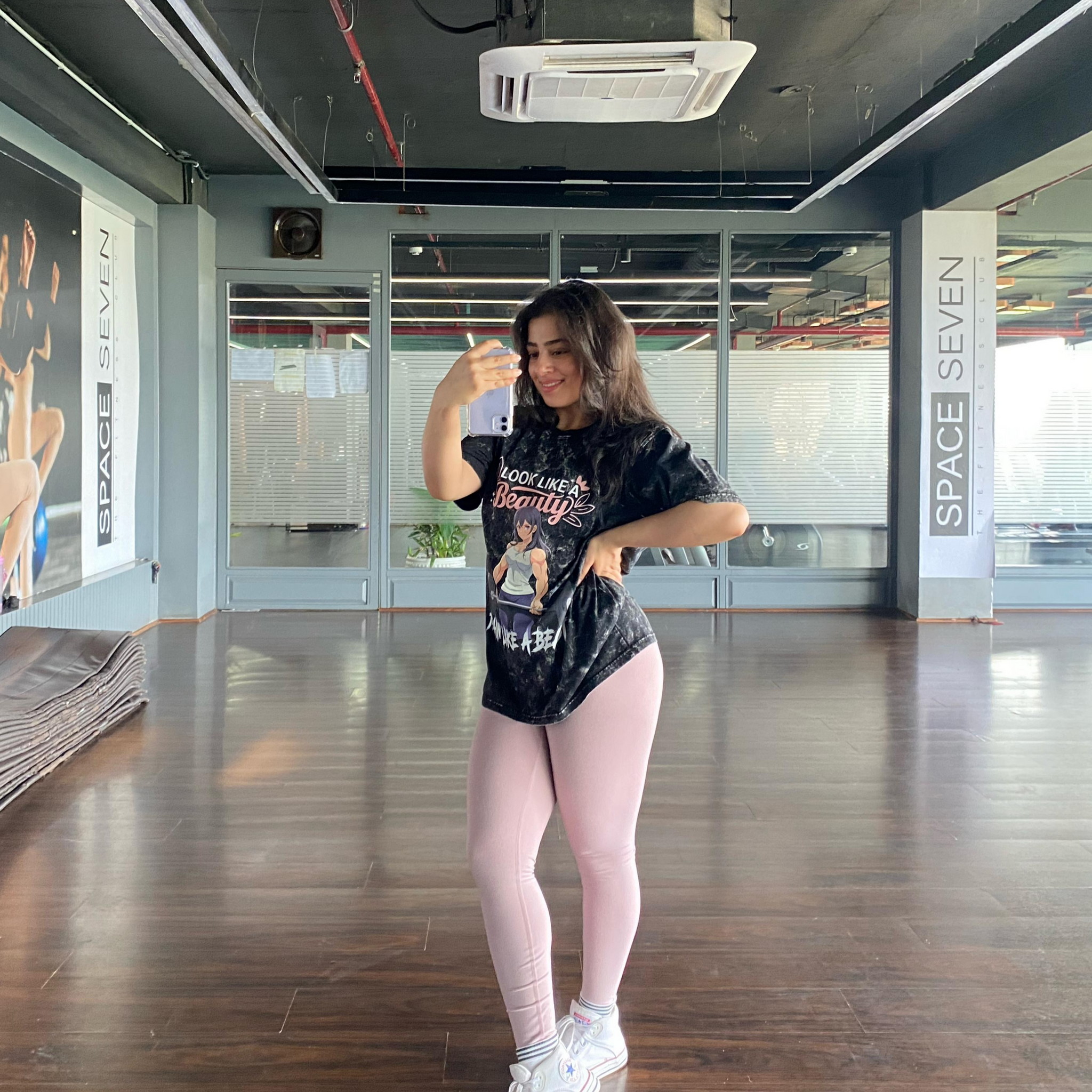Woman posing in a dance studio wearing the Manmaker t-shirt and pink leggings.